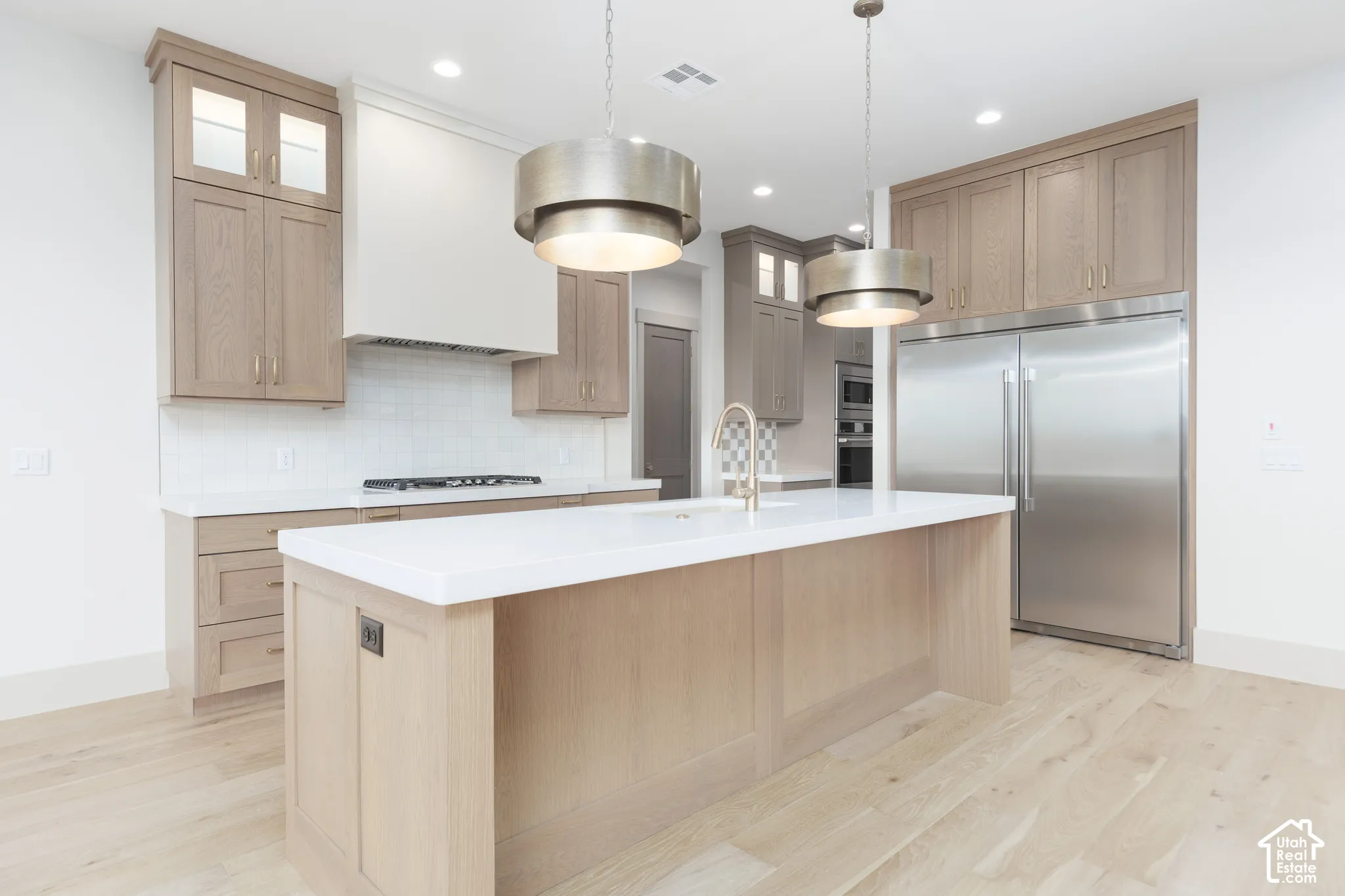 Kitchen featuring custom wood-finish cabinetry, a white stone island countertop, brushed metal pendant lighting, a stainless steel side-by-side refrigerator, and wide-plank wood-finish flooring