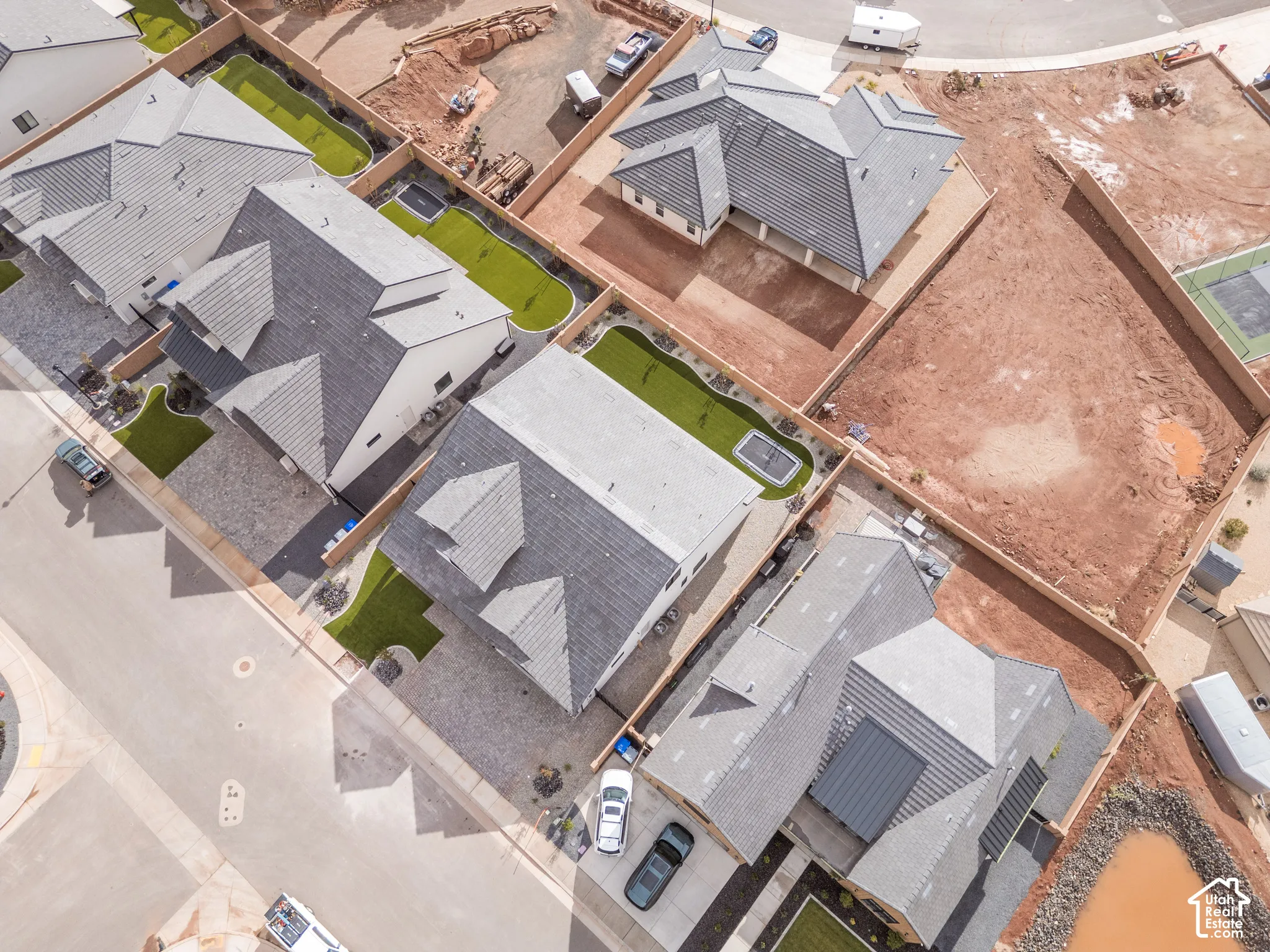 Aerial view of a residential neighborhood featuring multi-pitched shingled roofing, paved driveways, and maintained green space within fenced backyards