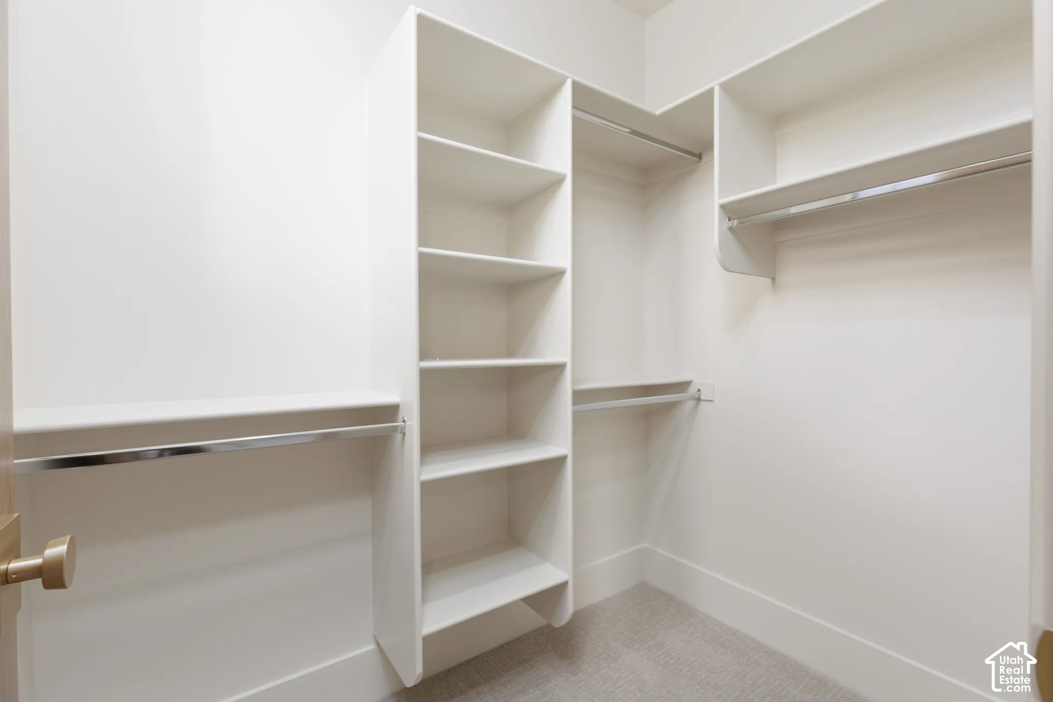 Custom storage closet featuring white laminate shelving, metal hanging rods, and neutral carpeting