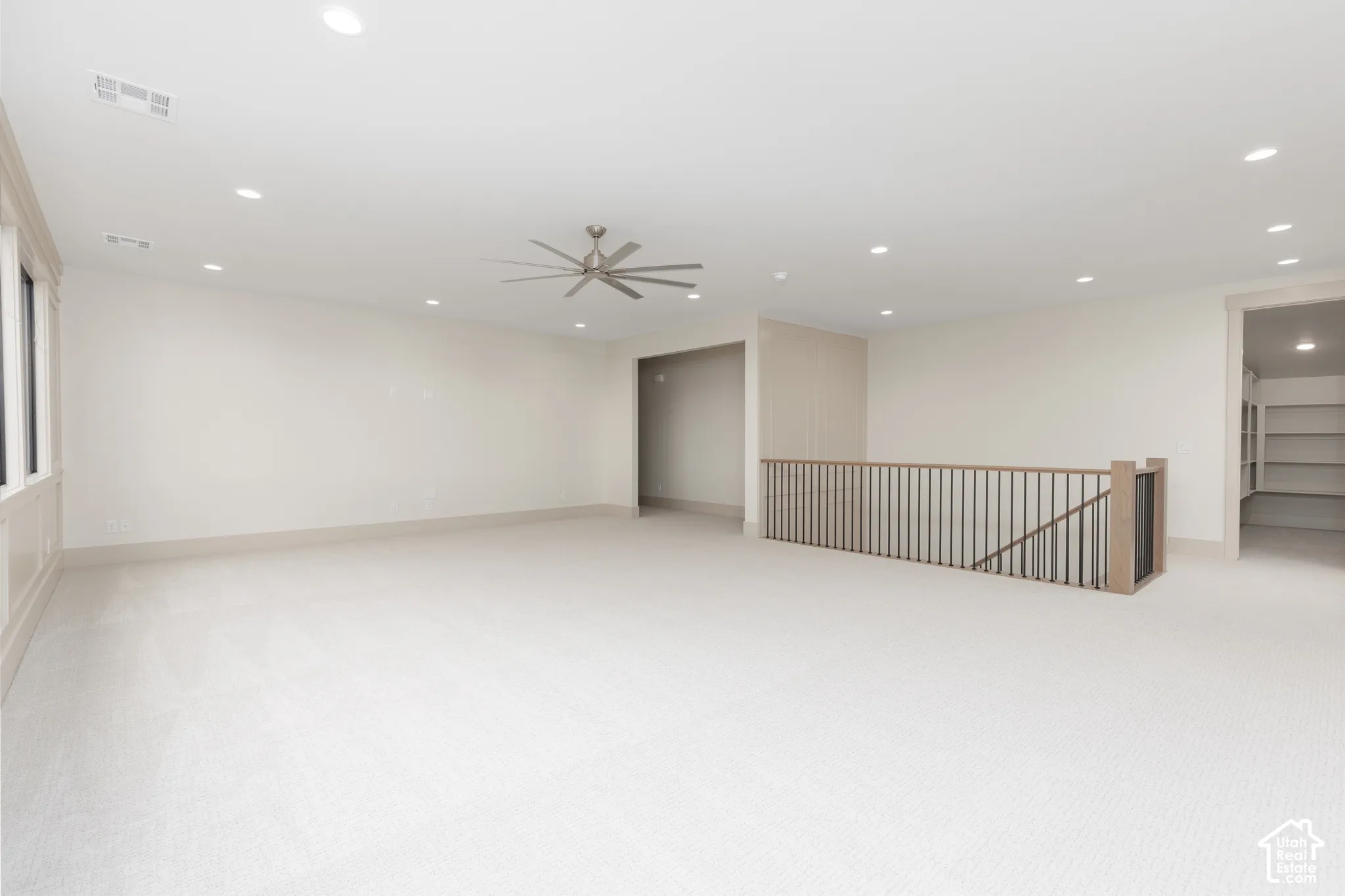 Expansive room featuring recessed lighting, a multi-blade ceiling fan, neutral wall-to-wall carpeting, and a custom metal and wood staircase railing
