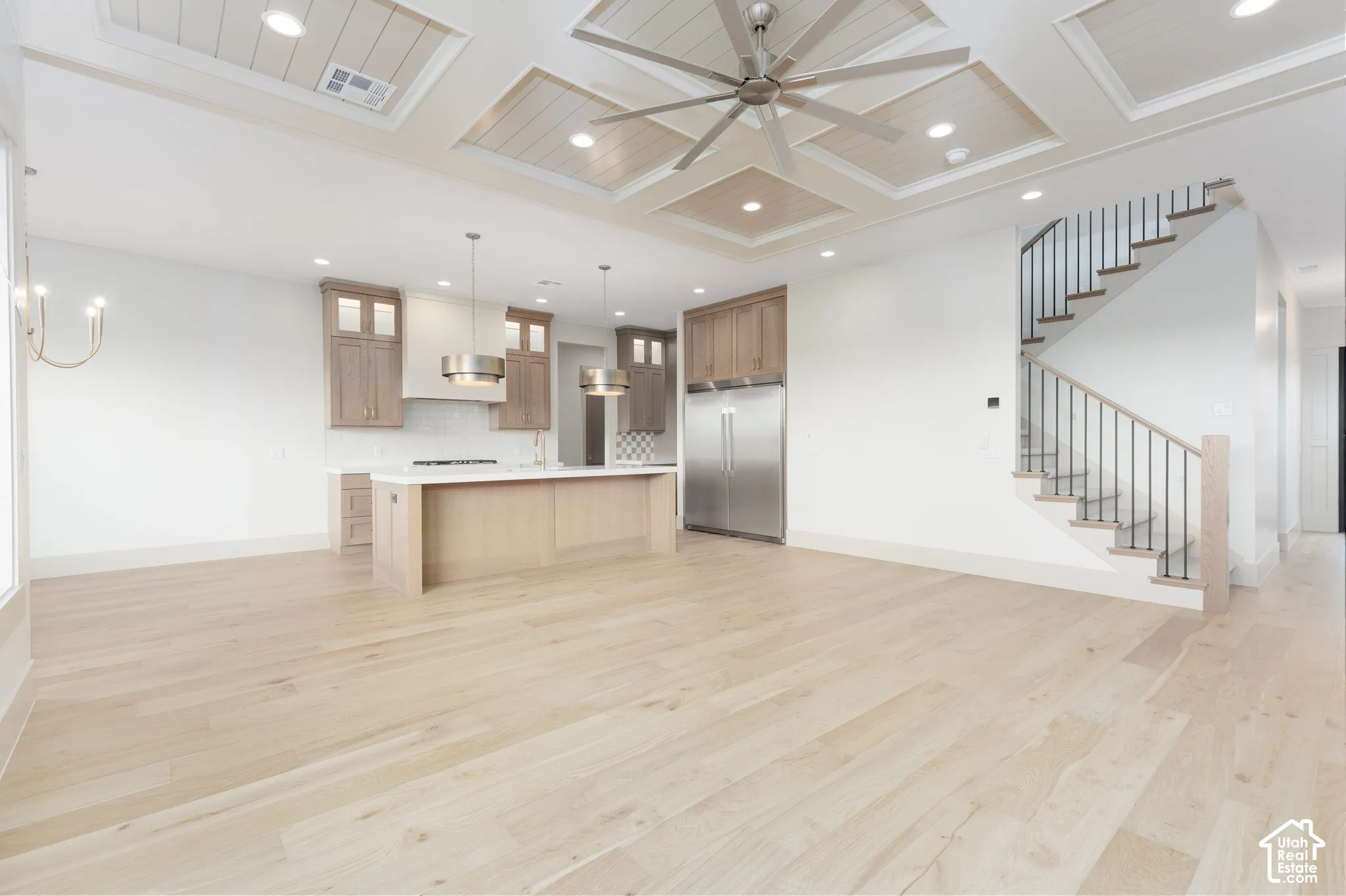 Coffered ceiling with paneled inlay, wood-finish flooring, custom cabinetry, stainless steel refrigerator, and staircase with metal railings