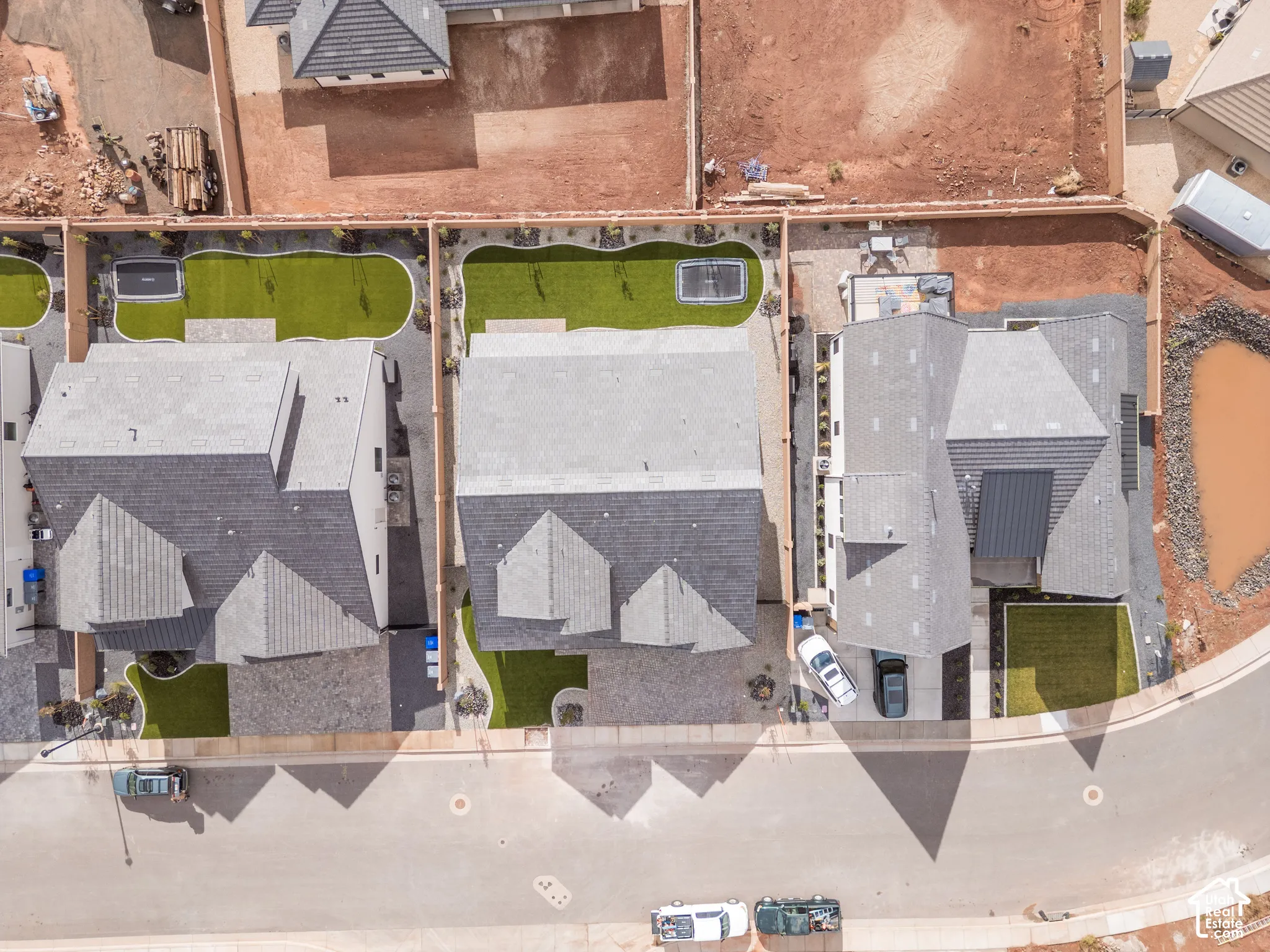 Aerial view of residential properties featuring shingled roofs, private driveways, fenced rear perimeters, and low-maintenance synthetic turf landscaping