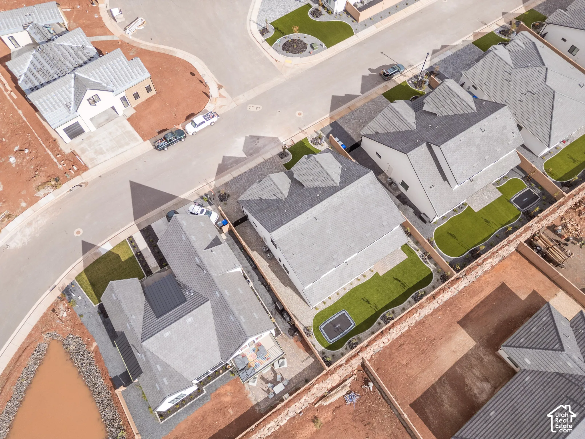 Aerial perspective featuring residential structures with pitched asphalt shingle roofing, manicured lawn areas, paved concrete driveways, and perimeter fencing