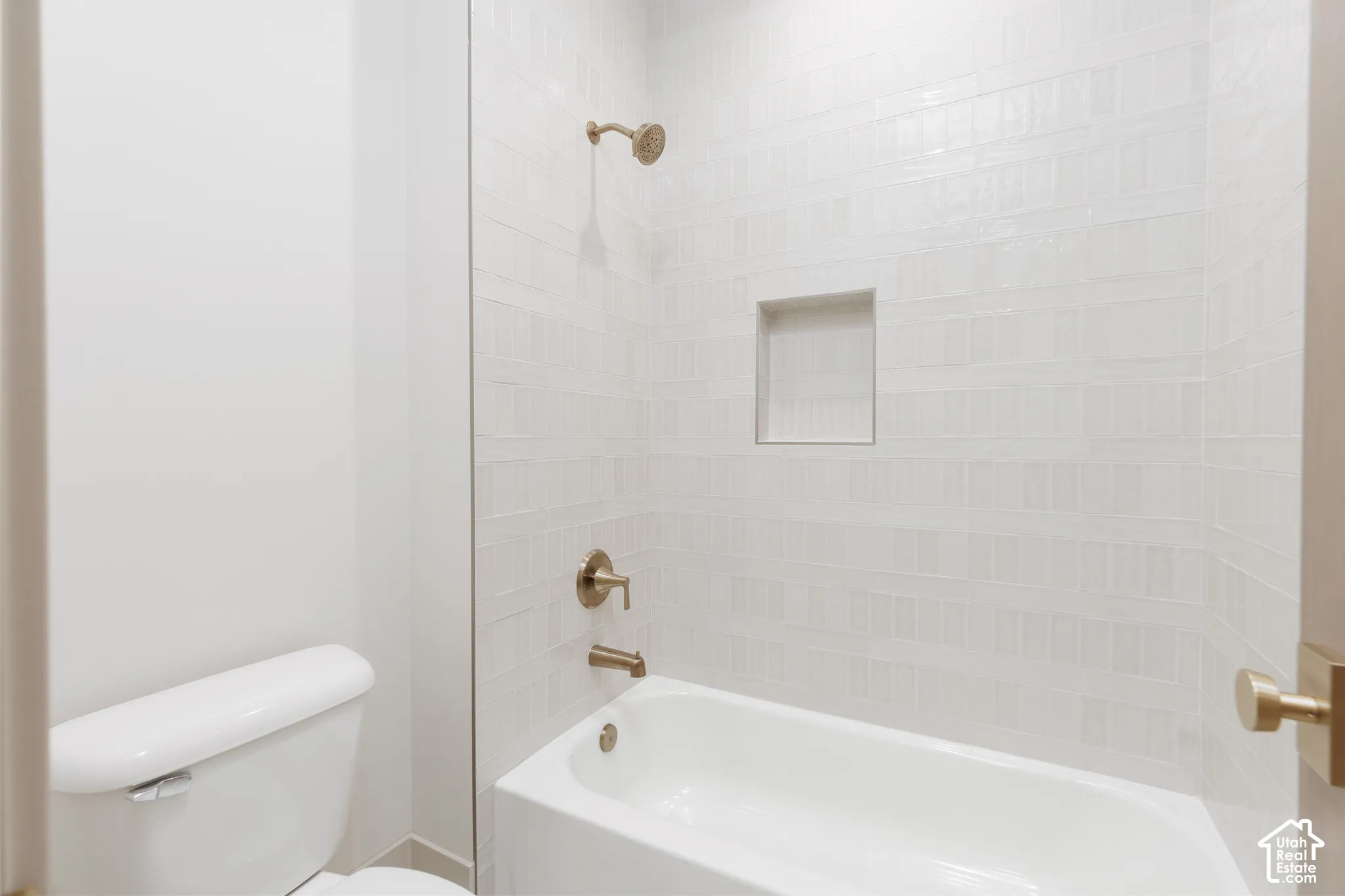 Bathroom featuring a tub-shower combination with white subway-style wall tile, a recessed storage niche, and metallic-finish hardware
