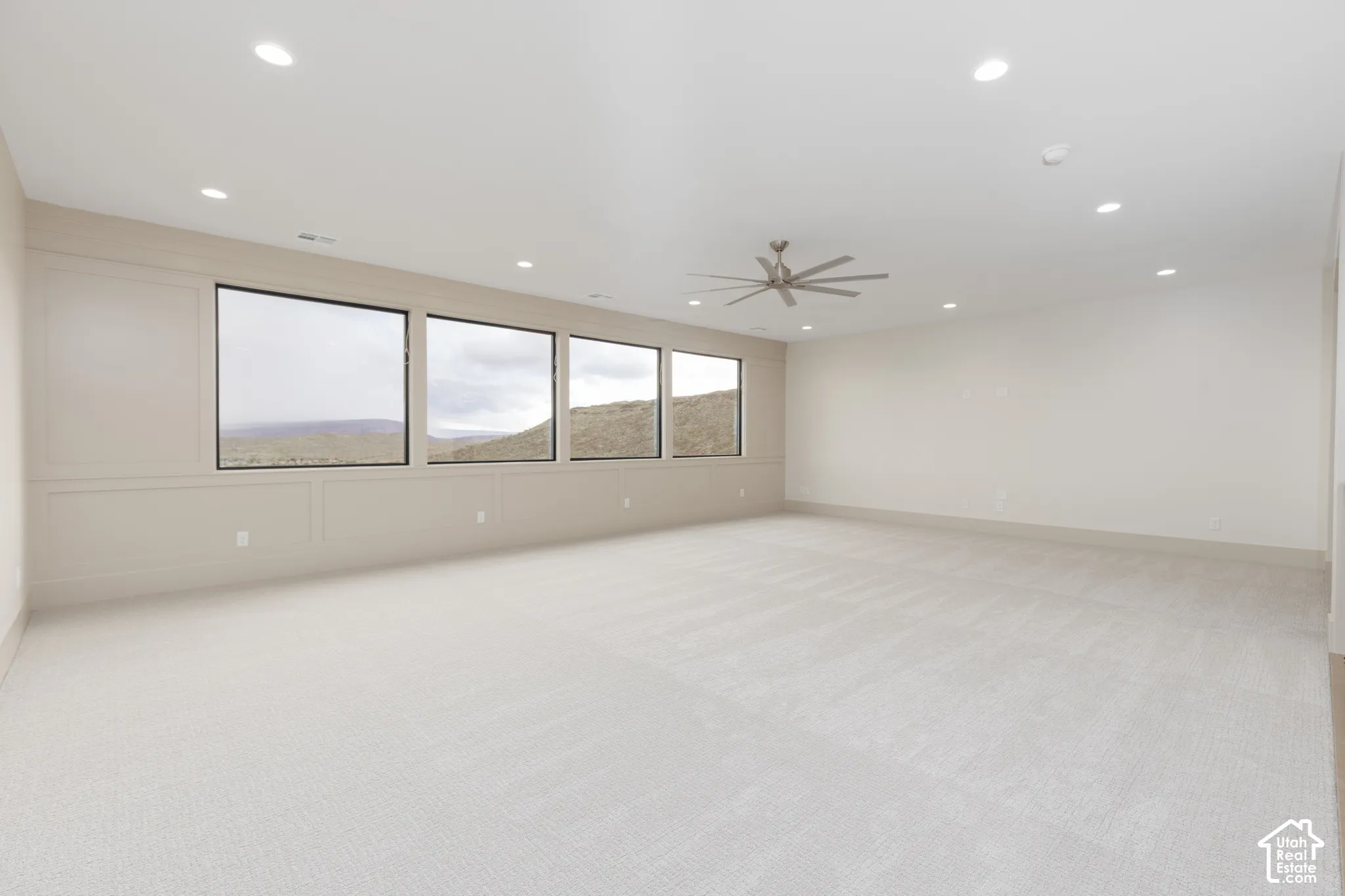 Spacious room featuring wall paneling, a row of large windows, neutral carpeting, recessed lighting, and a ceiling fan