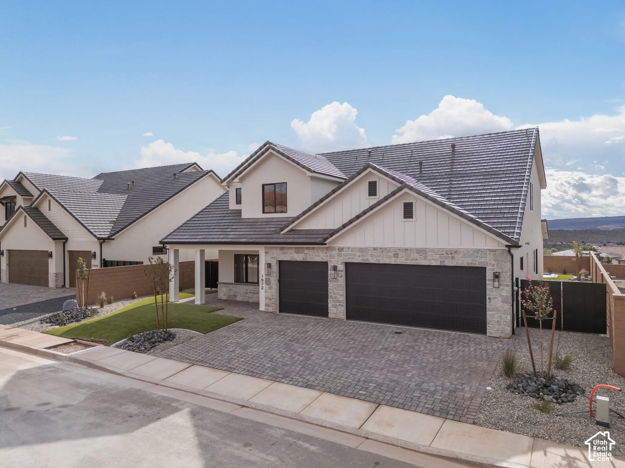 Two-story exterior featuring a stone veneer facade, vertical siding accents, a tile roof, a three-car garage, and a paver driveway