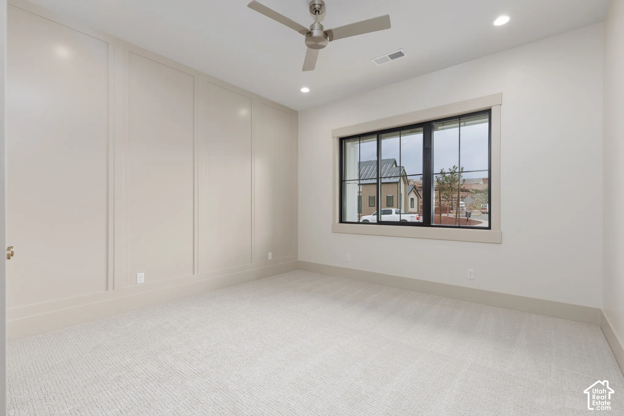 Room featuring neutral-toned wall paneling, multi-pane window with dark trim, neutral wall-to-wall carpeting, recessed lighting, and a metal ceiling fan