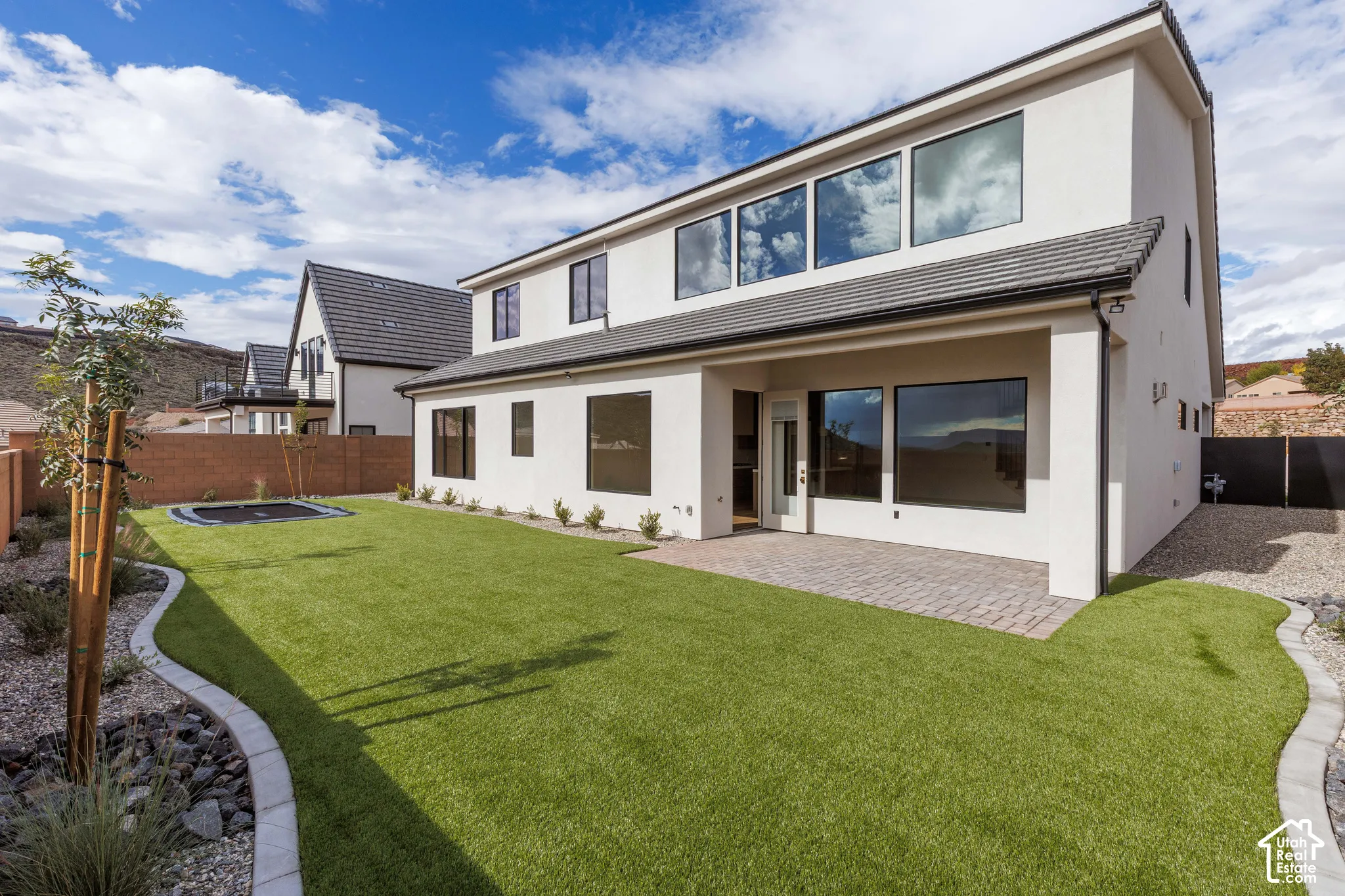 Stucco exterior featuring a covered patio, paved hardscaping, landscaped perimeter, and synthetic lawn
