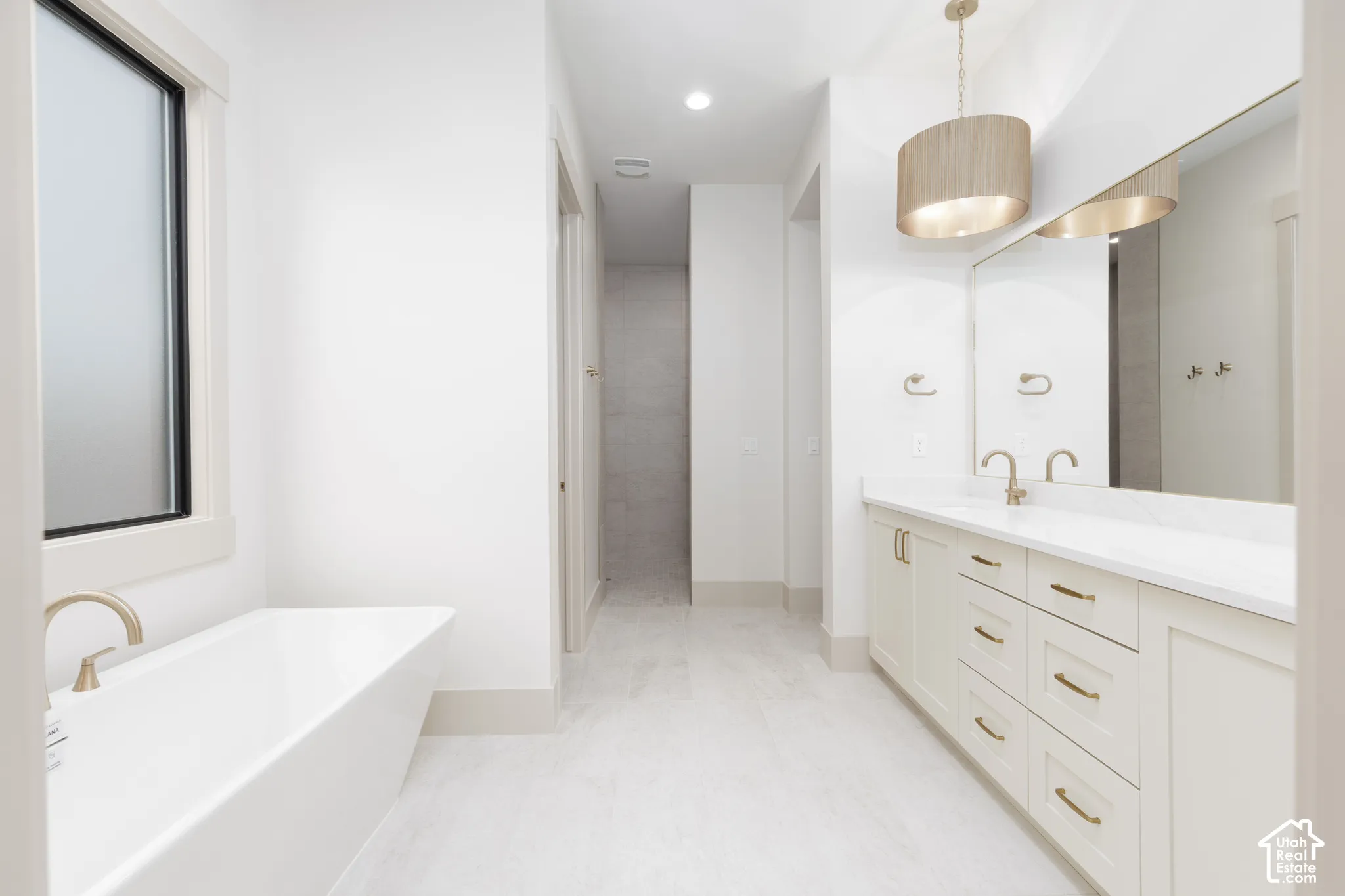Freestanding soaking tub with a wall-mounted faucet, dual-sink vanity with quartz countertop, full-width vanity mirror, and drum pendant lighting