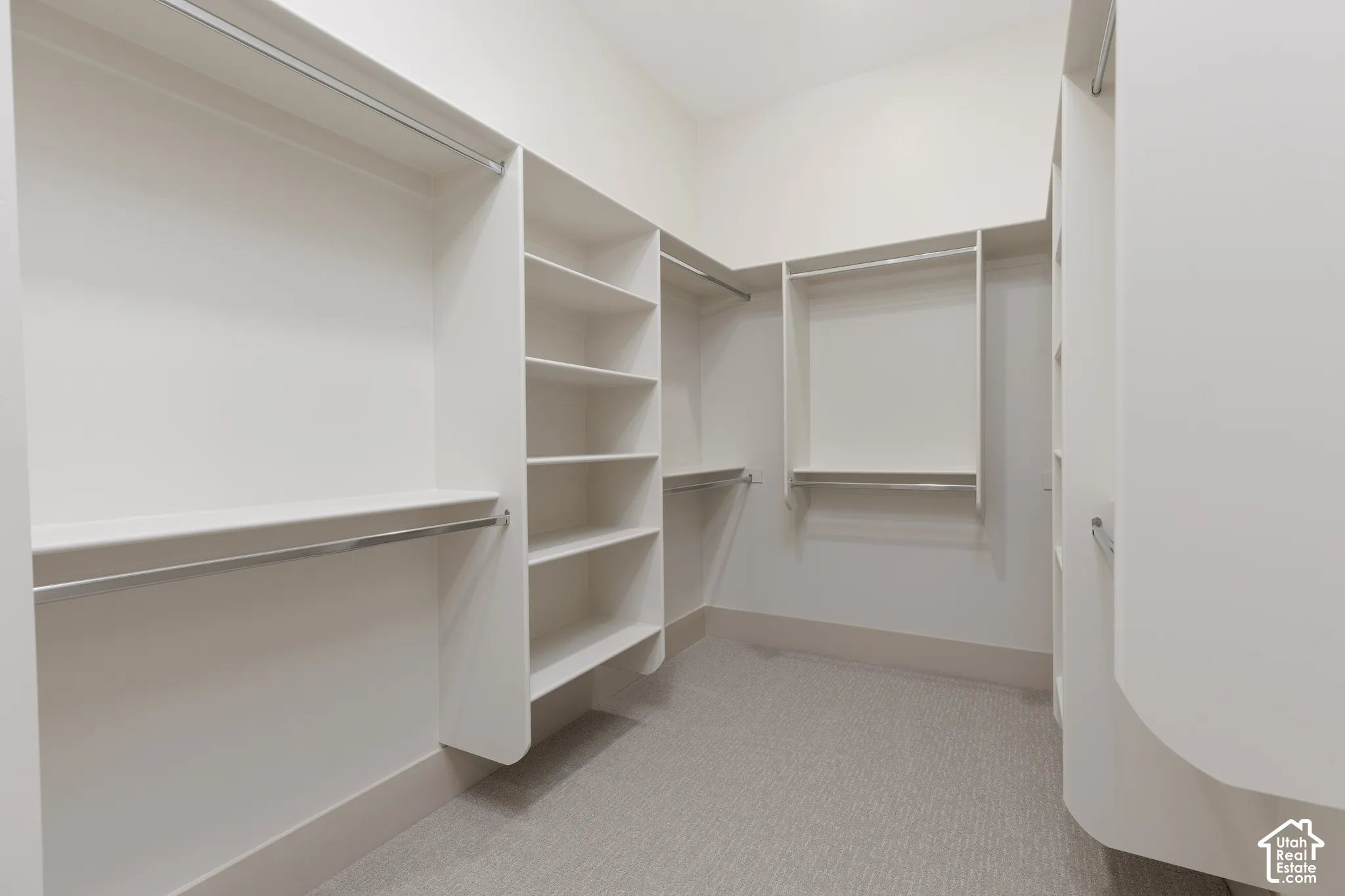Custom walk-in closet featuring white built-in shelving, multiple hanging rods, and neutral carpeting
