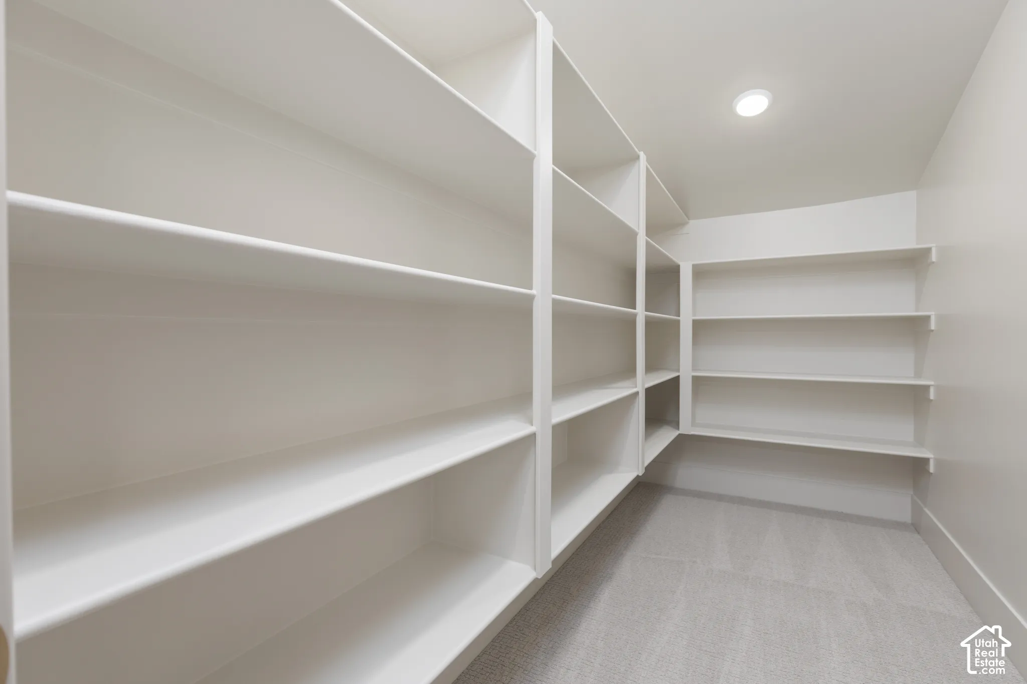 Walk-in storage space featuring multi-tier built-in shelving, recessed ceiling lighting, and wall-to-wall carpeting