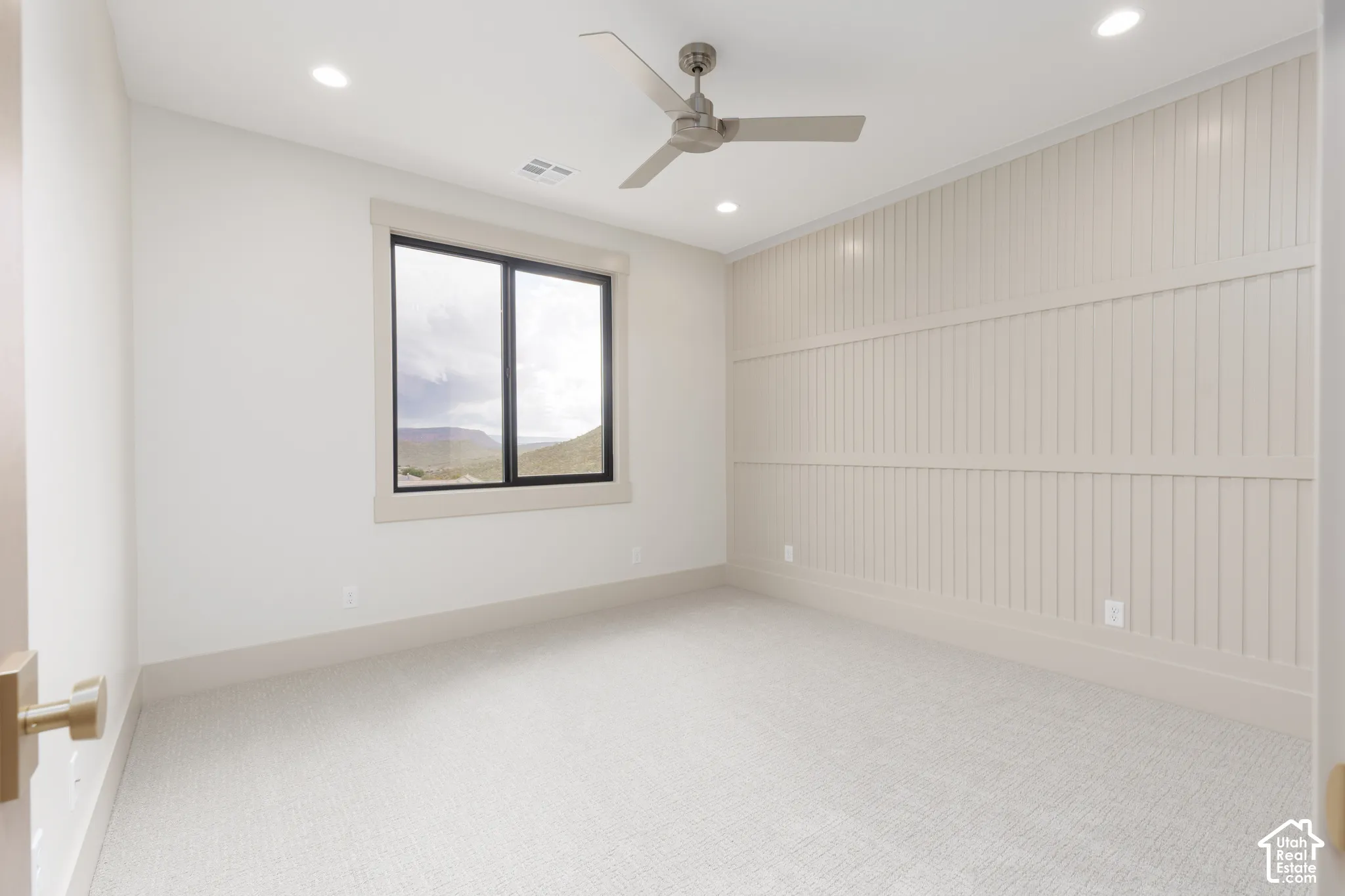 Interior space featuring a vertical slat accent wall, neutral carpeting, recessed lighting, a modern three-blade ceiling fan, and a window with mountain scenery
