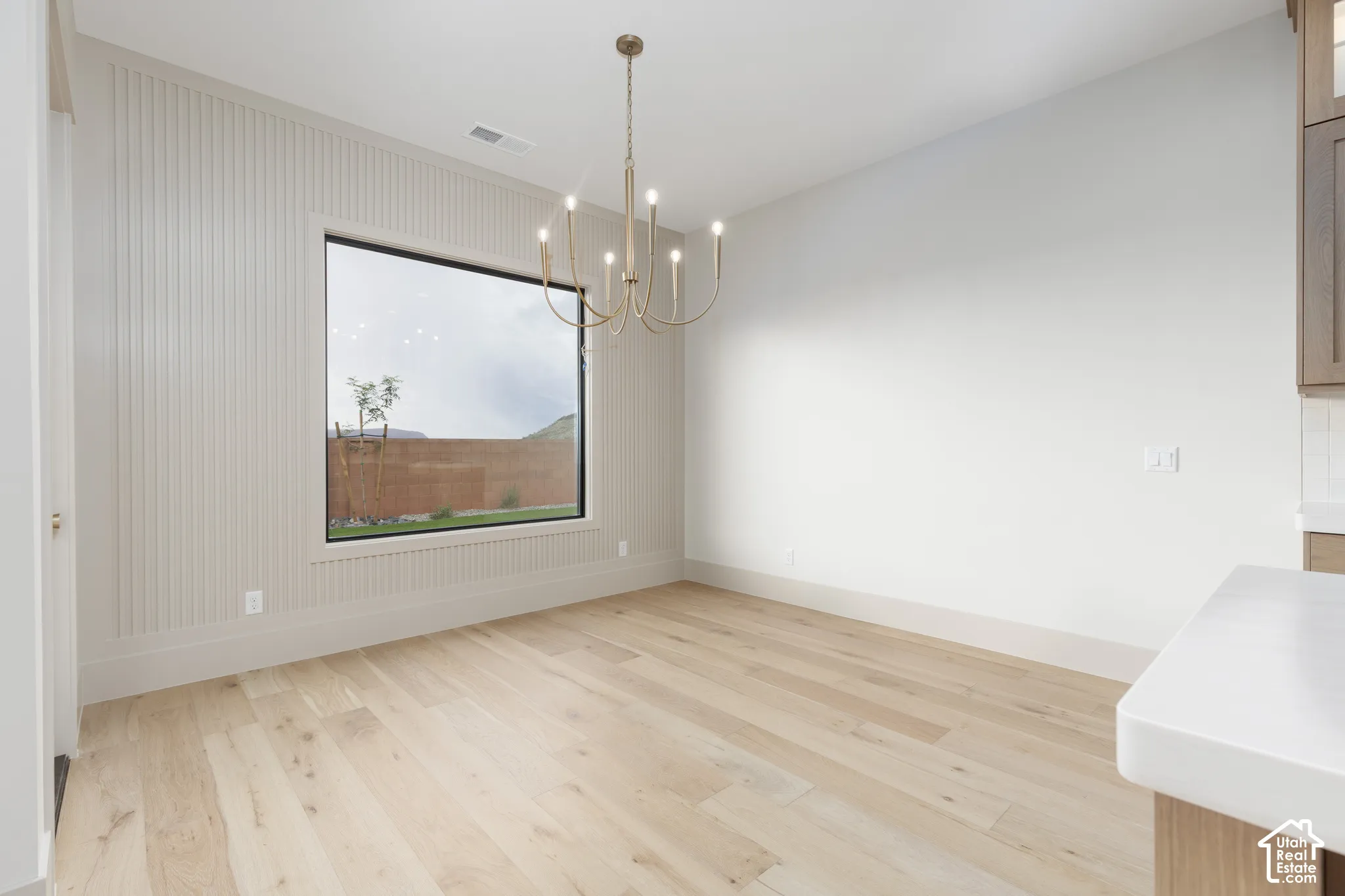 Interior space featuring wood-finish flooring, floor-to-ceiling vertical slat wall detailing, a large picture window, and a multi-arm metallic chandelier