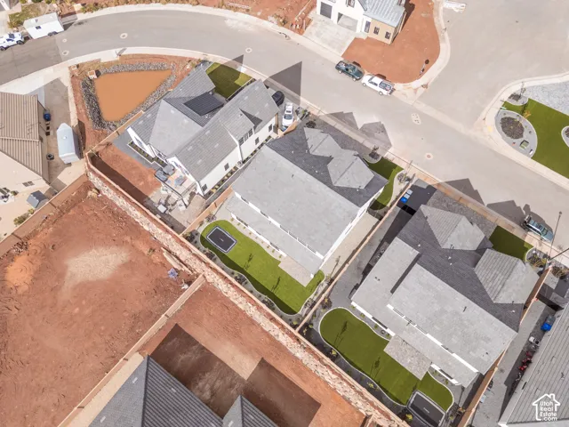 Aerial view of residential property featuring a multi-story structure with a pitched shingle roof, a fenced backyard with artificial turf, and a concrete patio