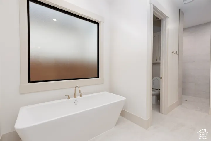 Freestanding soaking tub with a wall-mounted faucet, frosted picture window, tiled flooring, and an enclosed walk-in shower with floor-to-ceiling tile