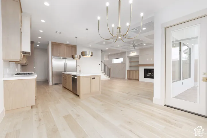 Open-concept interior featuring light wood-finish flooring, a kitchen island with stone countertops, a coffered ceiling, a stone-surround fireplace, and custom built-in cabinetry