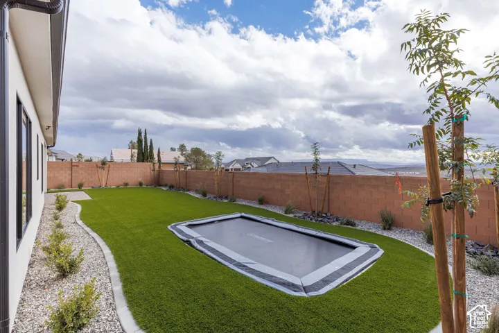 Private backyard featuring a synthetic lawn, in-ground trampoline, perimeter masonry wall, and decorative gravel borders