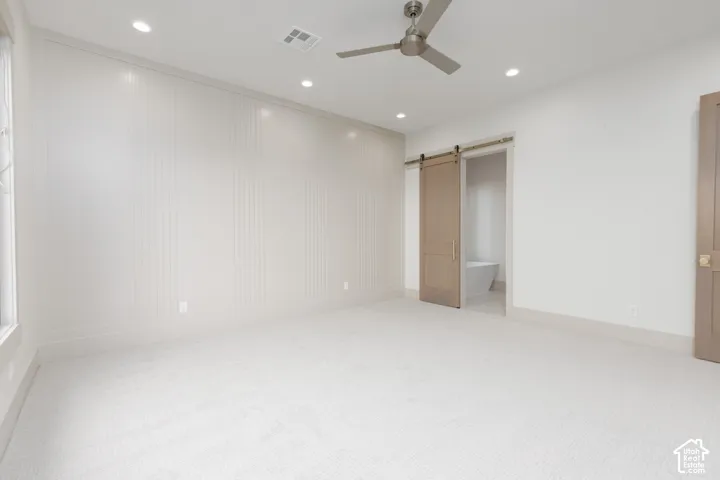 Neutral-toned room featuring a decorative paneled accent wall, recessed lighting, ceiling fan, carpeted flooring, and a sliding barn-style door