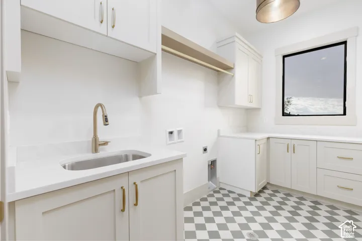 Laundry room featuring shaker-style cabinetry, solid-surface countertops, an undermount sink with a gooseneck faucet, a built-in hanging rod, and checkered tile flooring