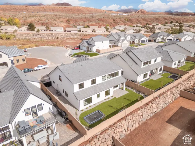Two-story residential structure featuring a white stucco exterior, pitched shingle roof, rear patio, and a landscaped backyard enclosed by masonry perimeter walls