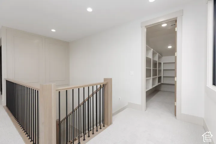 Staircase featuring wood handrails, metal balusters, and wainscoting paneling, accompanied by a walk-in storage area with built-in shelving