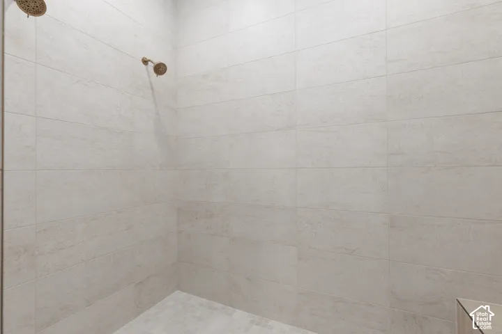 Walk-in shower featuring large-format light-toned tile wall surround, mosaic tile floor, and dual metallic finish showerheads