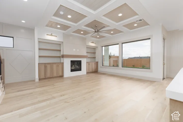 Coffered ceiling with wood-panel inlay, light wood-finish flooring, fireplace with wood mantel, custom built-in cabinetry, and large windows