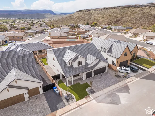 Modern multi-gabled residence featuring a tiled roof, white exterior cladding, attached two-car garage, and low-maintenance synthetic turf landscaping with stone accents