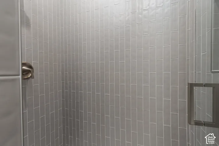 Shower enclosure featuring vertical light-gray subway tile, satin-finish metal plumbing fixtures, and a glass door with a square metal handle