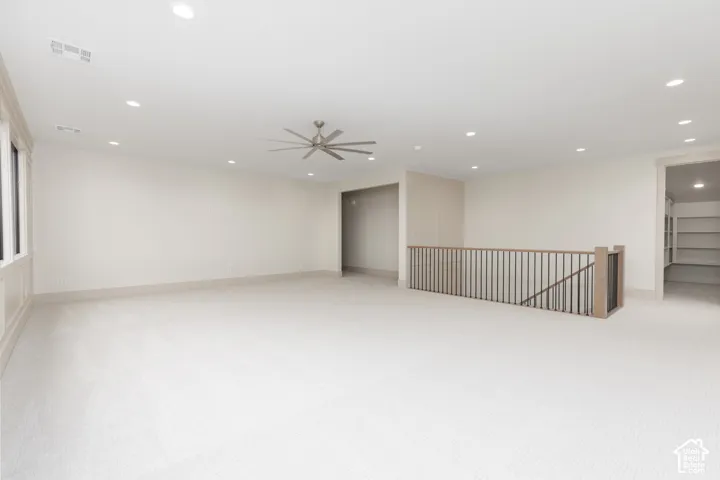Expansive room featuring recessed lighting, a multi-blade ceiling fan, neutral wall-to-wall carpeting, and a custom metal and wood staircase railing