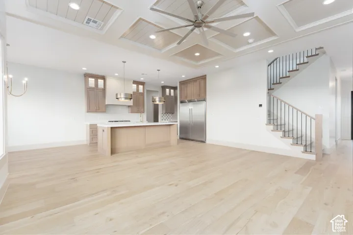 Coffered ceiling with paneled inlay, wood-finish flooring, custom cabinetry, stainless steel refrigerator, and staircase with metal railings