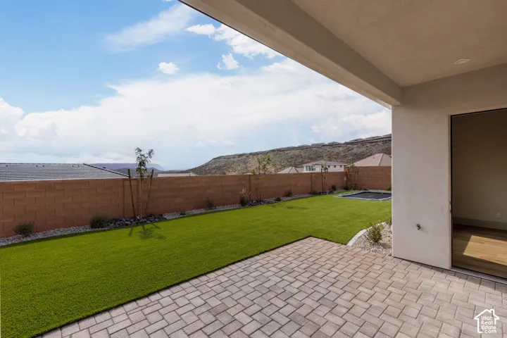 Covered patio with stone paver flooring, synthetic grass lawn, masonry privacy wall, and desert mountain backdrop
