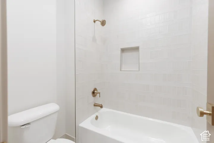 Bathroom featuring a tub-shower combination with white subway-style wall tile, a recessed storage niche, and metallic-finish hardware