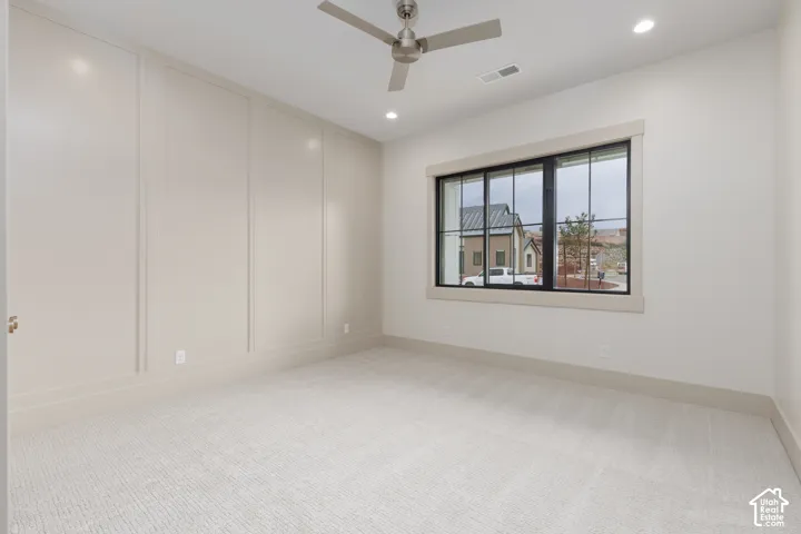 Room featuring neutral-toned wall paneling, multi-pane window with dark trim, neutral wall-to-wall carpeting, recessed lighting, and a metal ceiling fan