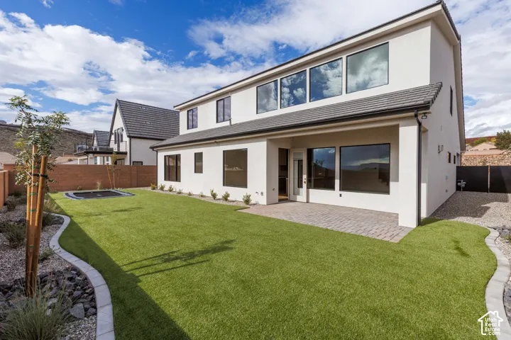 Stucco exterior featuring a covered patio, paved hardscaping, landscaped perimeter, and synthetic lawn