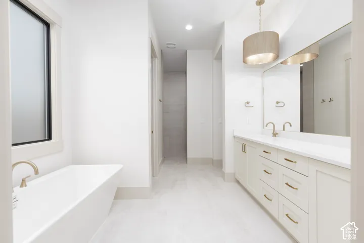 Freestanding soaking tub with a wall-mounted faucet, dual-sink vanity with quartz countertop, full-width vanity mirror, and drum pendant lighting