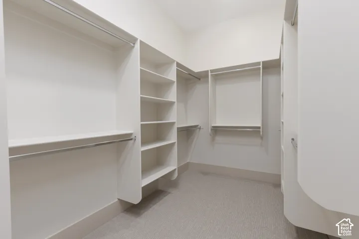 Custom walk-in closet featuring white built-in shelving, multiple hanging rods, and neutral carpeting