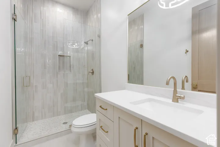 Bathroom featuring a vanity with a solid-surface countertop, gold-toned hardware, an integrated sink, vertical-patterned tile shower enclosure with a glass door, and a pebble-tiled shower floor
