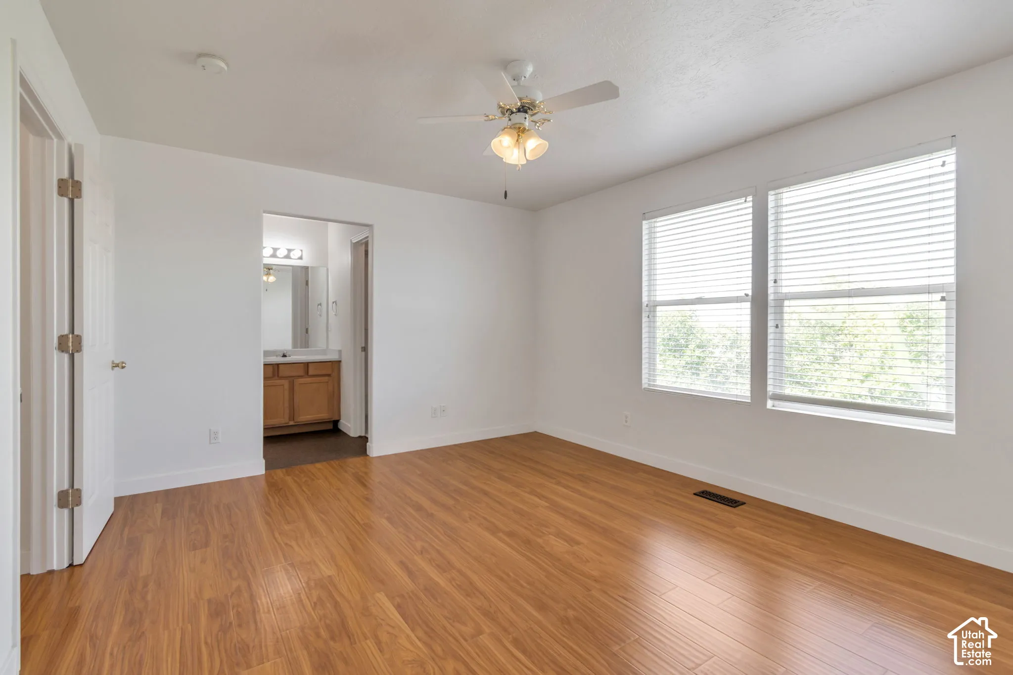 Room featuring wood-finish flooring, dual windows with horizontal blinds, and a ceiling fan with integrated lighting