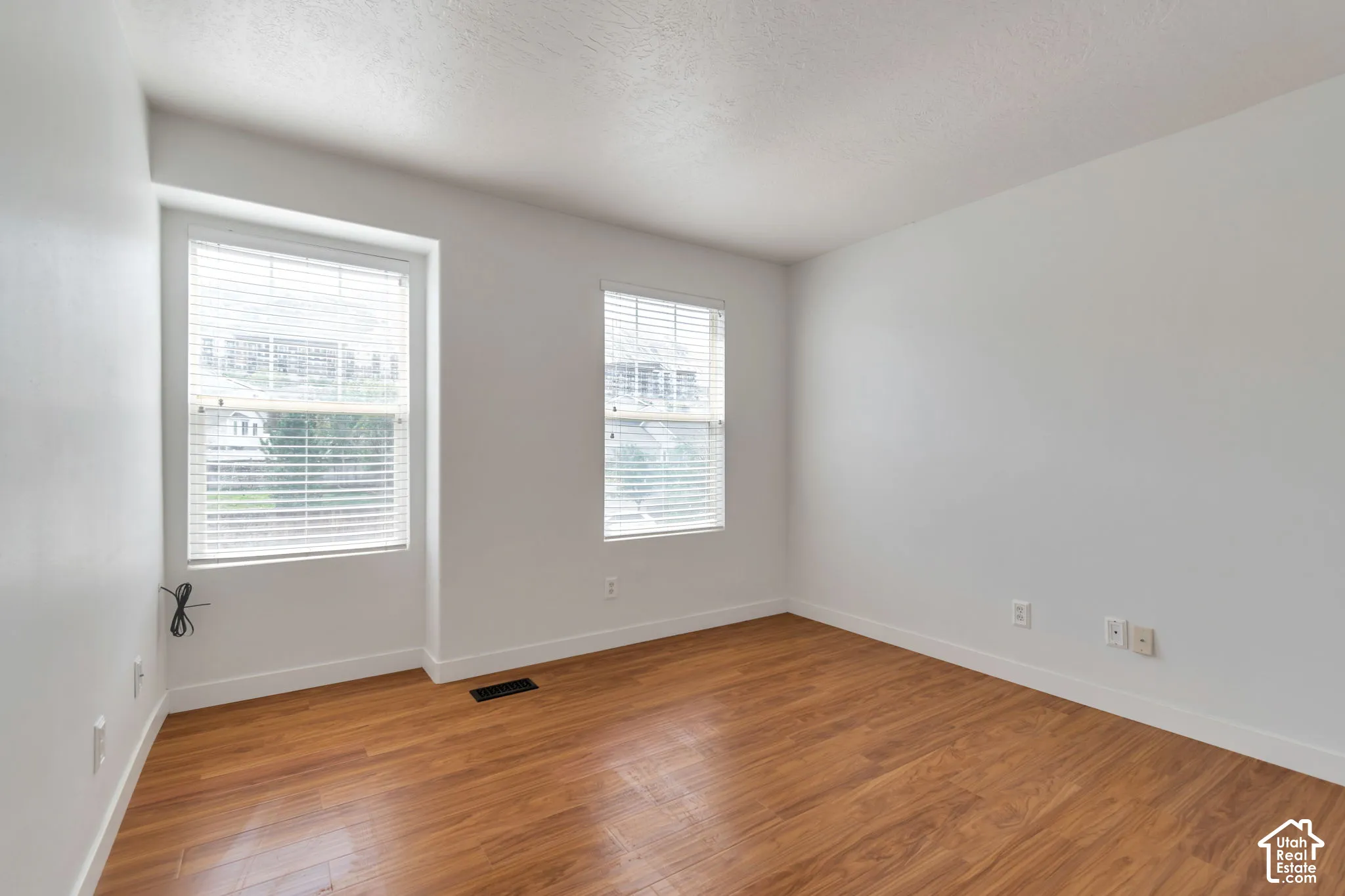 Room featuring wood-finish flooring, white walls, and two windows equipped with horizontal blinds