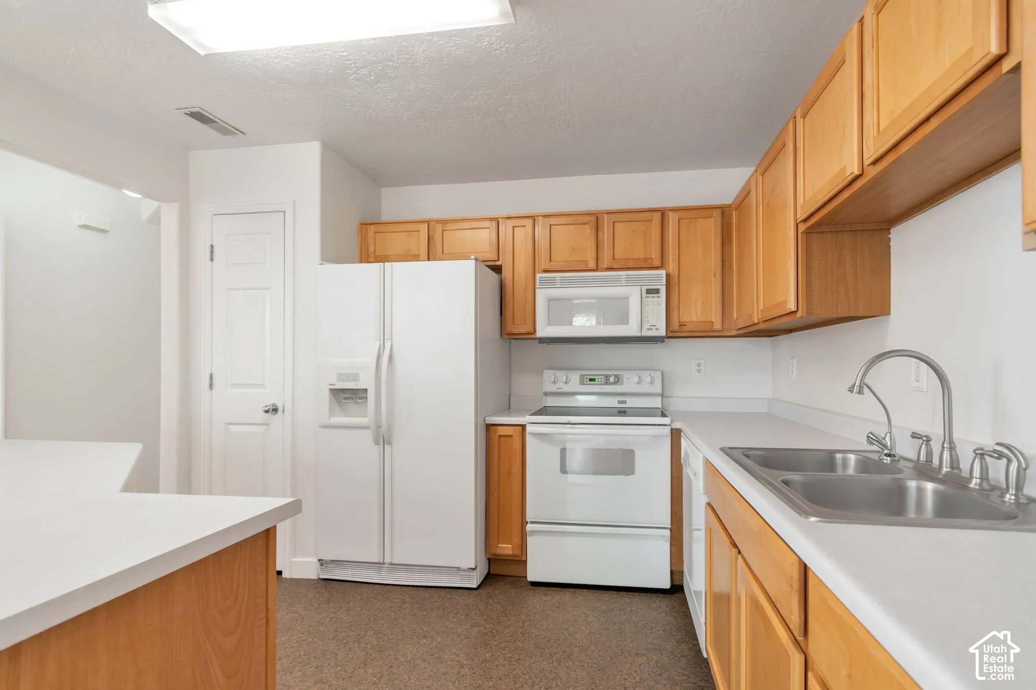 Kitchen featuring natural wood cabinetry, white appliances, solid-surface countertops, dual-basin stainless steel sink, and recessed lighting
