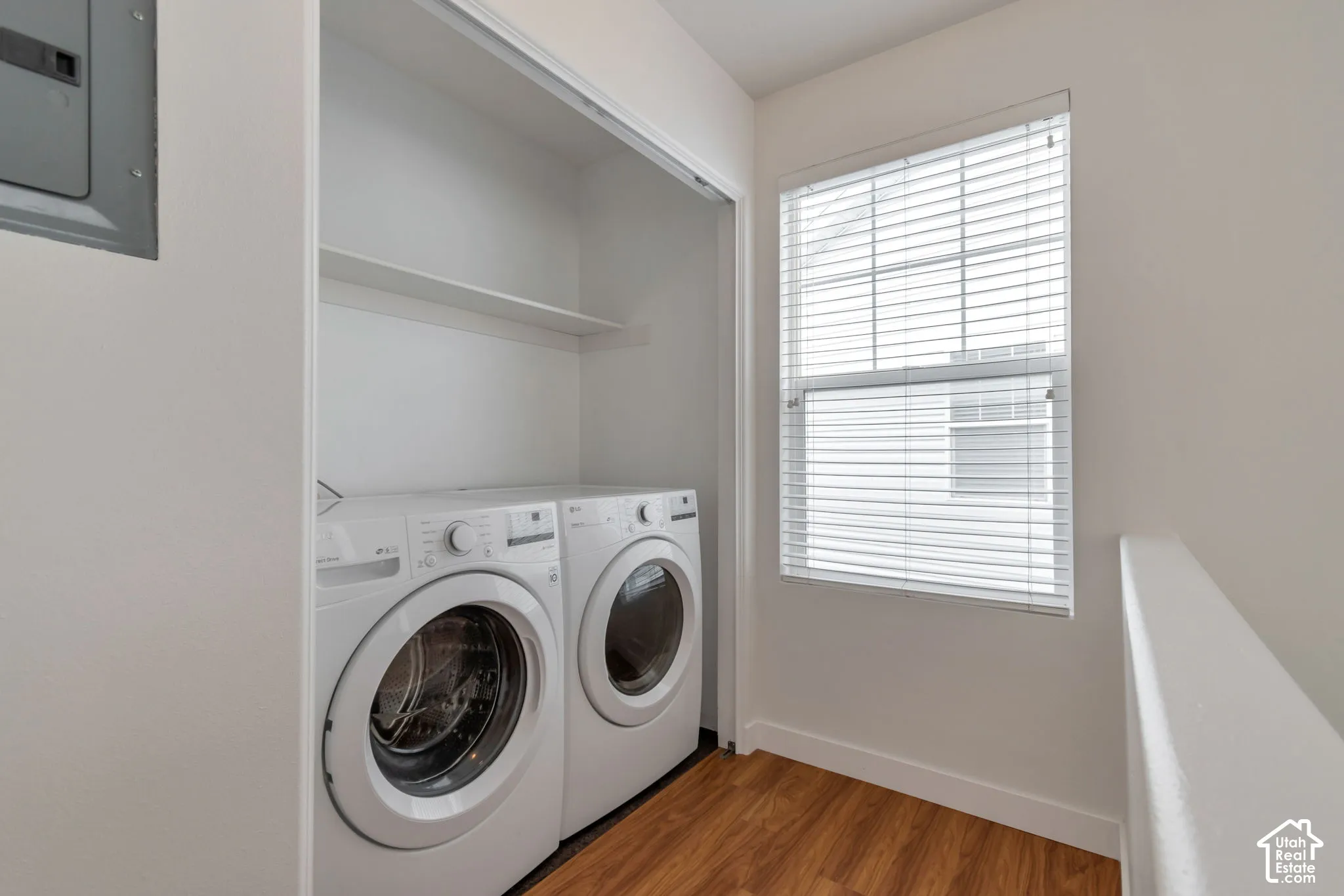Laundry area featuring wood-finish flooring, a built-in overhead shelf, and a window equipped with horizontal blinds