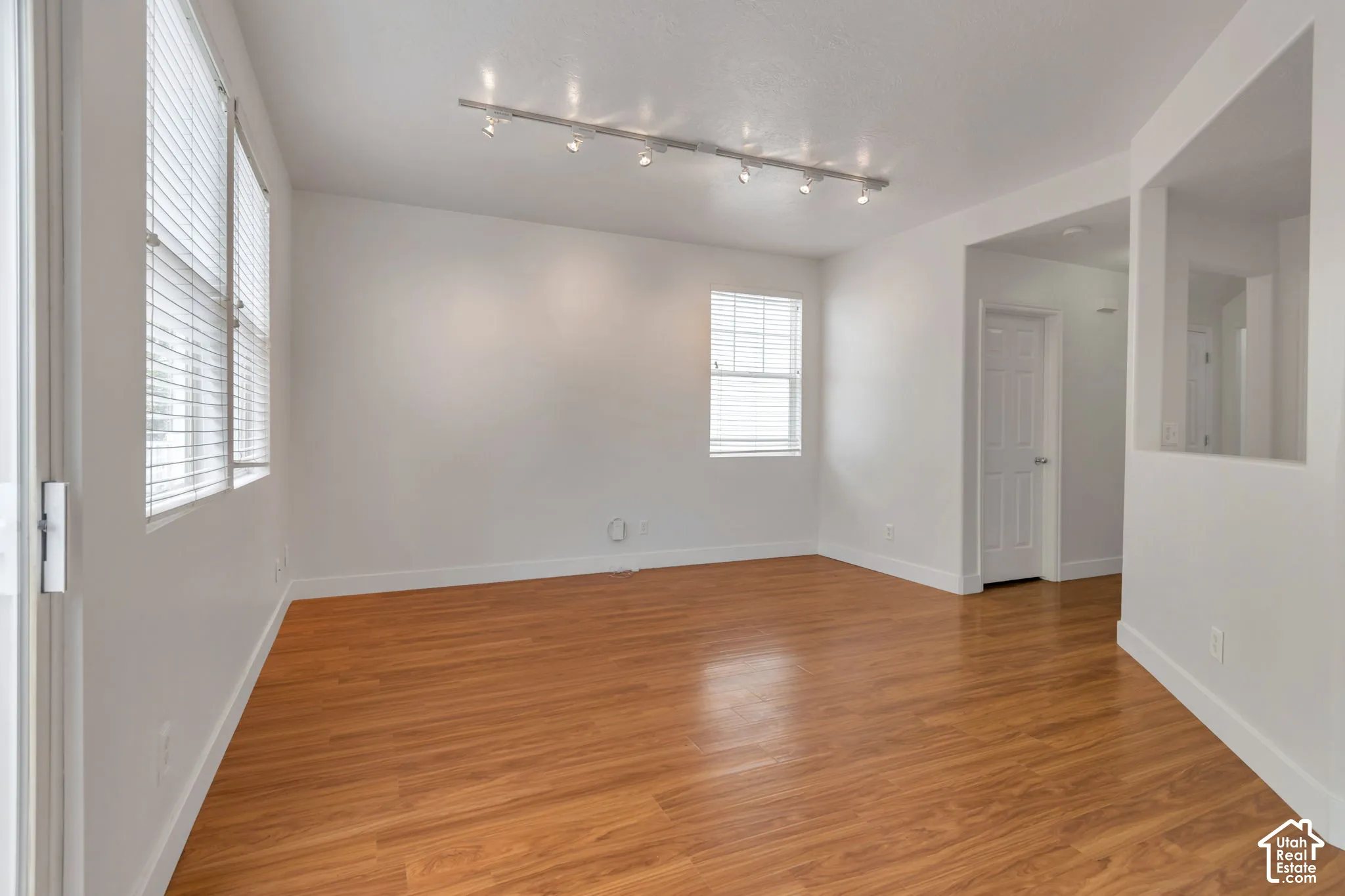 Interior space featuring wood-finish flooring, multi-light track lighting, white walls, and windows with horizontal blinds