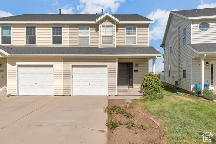 Two-story exterior featuring tan horizontal siding, asphalt shingle roofing, attached two-car garage, and concrete driveway