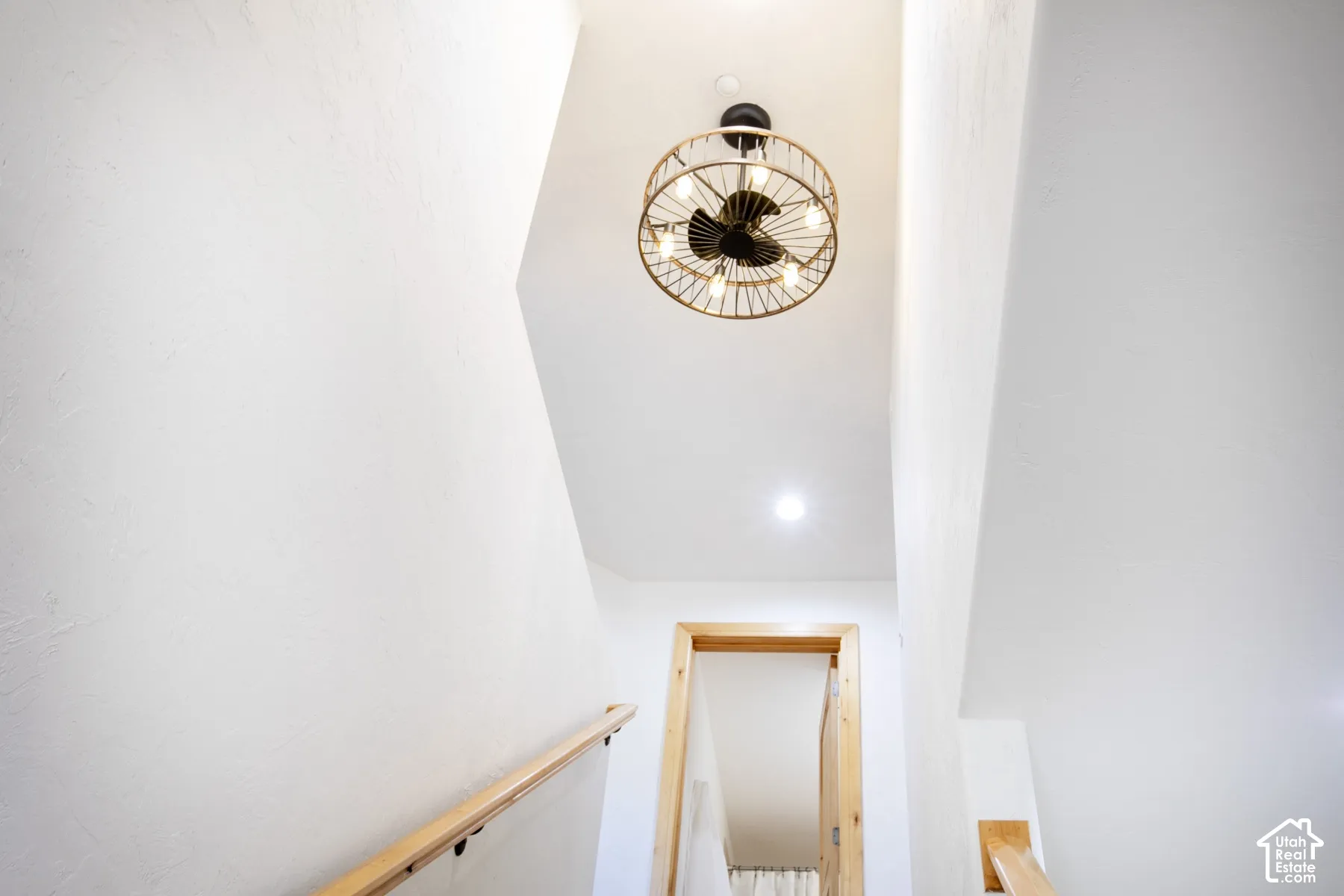 Cage-style ceiling fixture with exposed bulbs, light-toned wood handrails, and smooth white walls