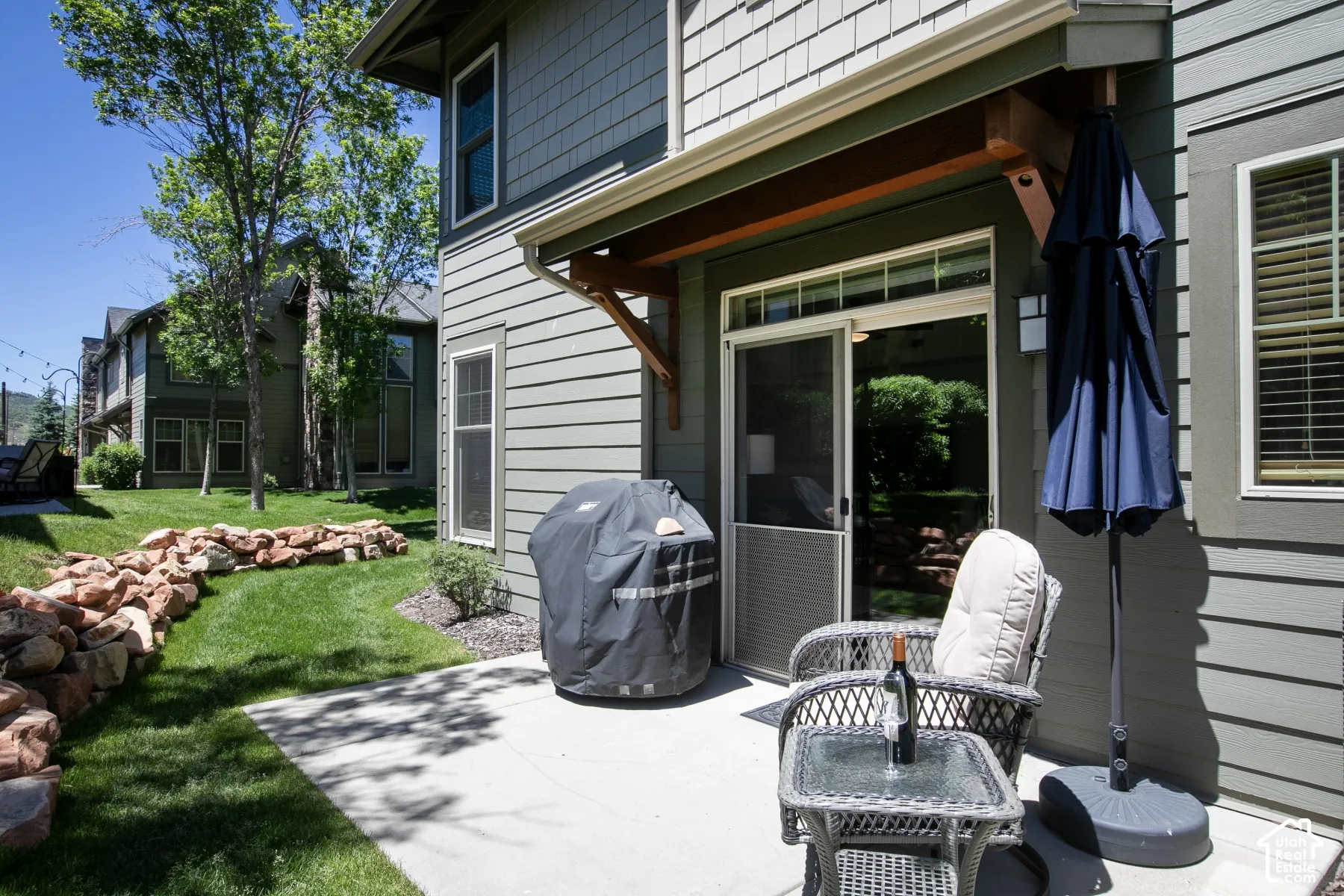 Concrete patio with wood-finish siding, natural stone retaining wall, and exterior wooden eave support