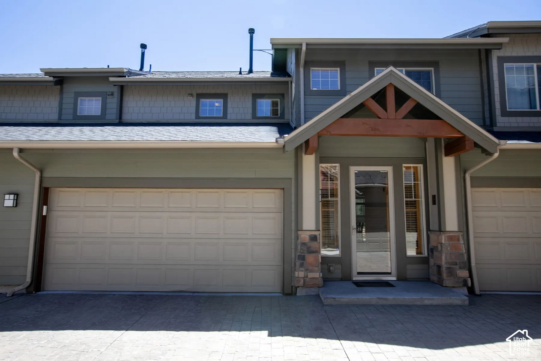 Exterior featuring horizontal and shingle-style siding, stone veneer column bases, a wood-trimmed entryway gable, and a multi-car garage with paneled doors