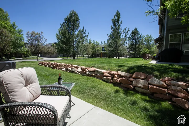 Backyard featuring a concrete patio, a natural stone retaining wall, and mature trees