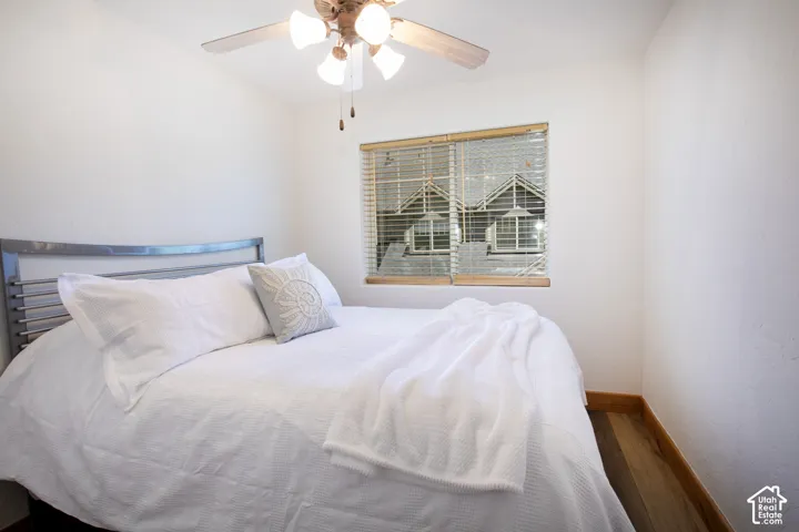 Interior room featuring wood-finish flooring, a ceiling fan with integrated lighting, and a window equipped with horizontal blinds
