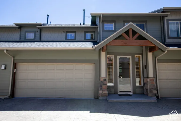 Exterior featuring horizontal and shingle-style siding, stone veneer column bases, a wood-trimmed entryway gable, and a multi-car garage with paneled doors